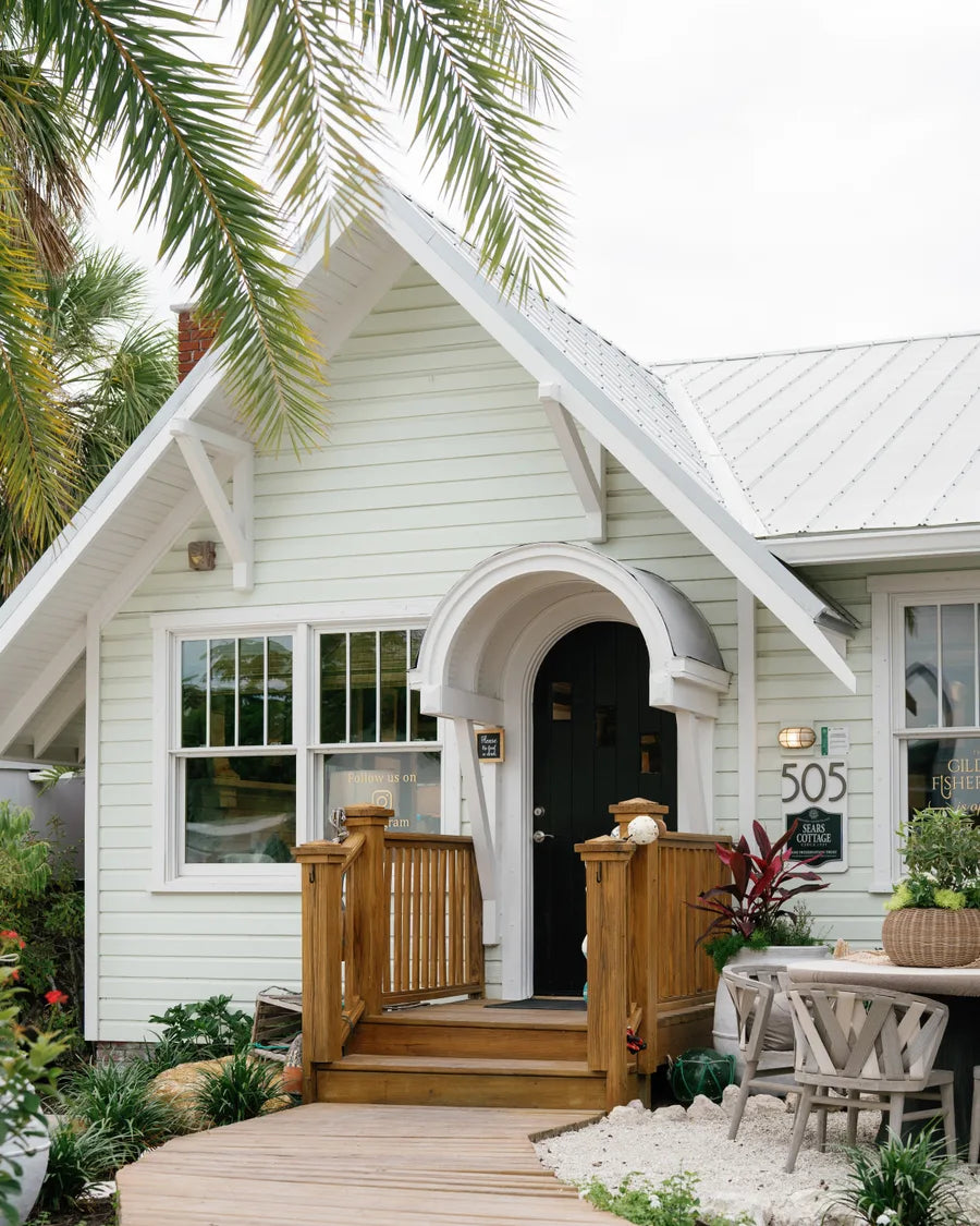The shop's front porch: an arched black door under a gabled portico, the number 505, framed by palms and a white picket fence