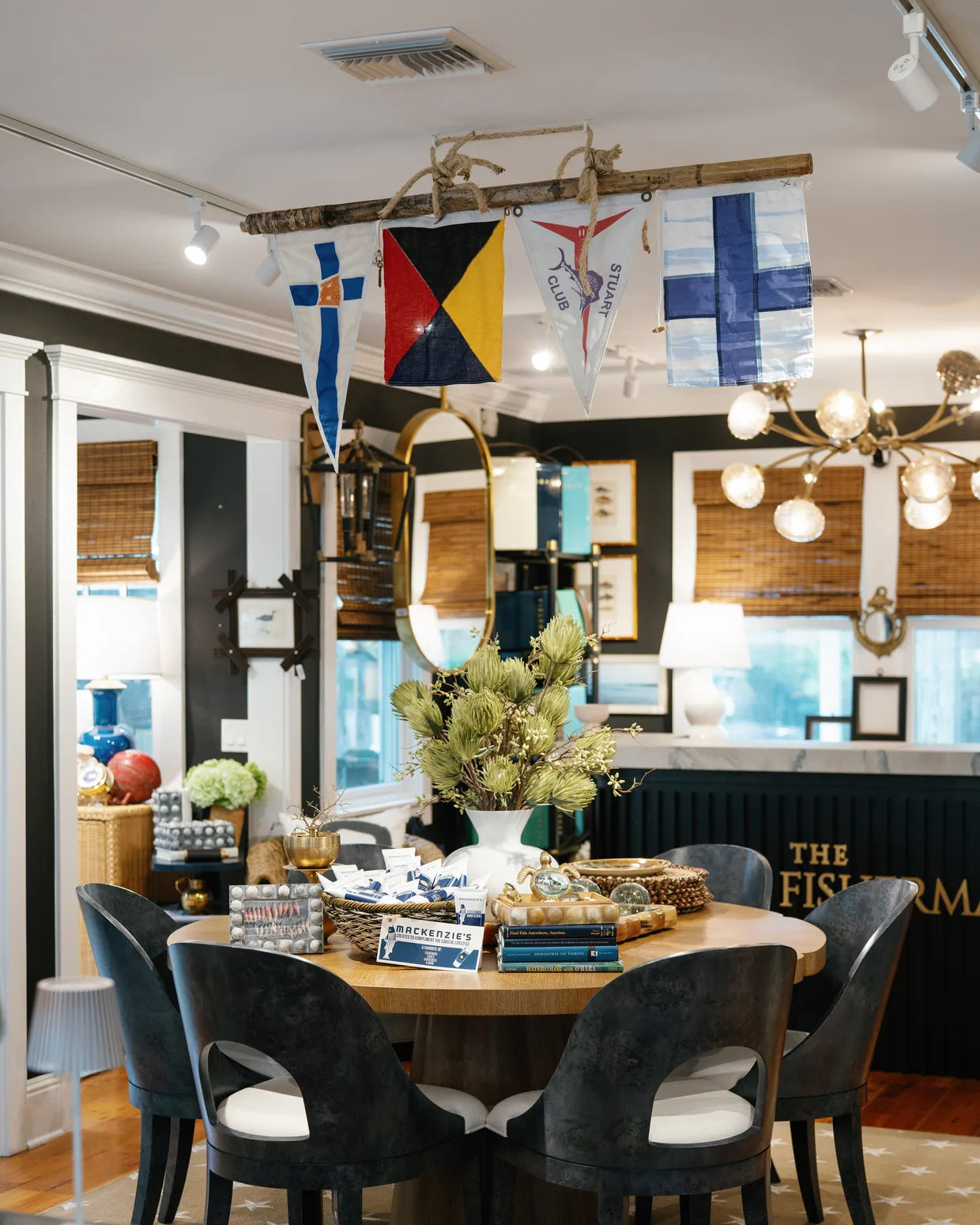 Inside the shop: a round table set beneath a string of nautical signal flags, dark chairs on a star-patterned rug, the marble counter and 'The Fisherman' sign beyond